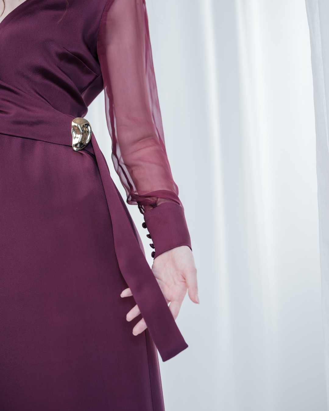Amethyst Grace Dress in rich burgundy features a golden zamak accessory, sheer sleeves, and silk-covered buttons for opulent sophistication at formal events.