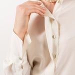 Close-up of ivory silk shirt, showcasing its soft silk texture, elegant shell buttons, and refined stitching.