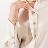 Close-up of ivory silk shirt, showcasing its soft silk texture, elegant shell buttons, and refined stitching.
