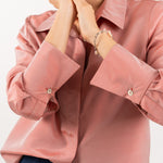 Close-up of peach pink silk shirt, showcasing the lustrous silk fabric, refined stitching, and delicate shell buttons.