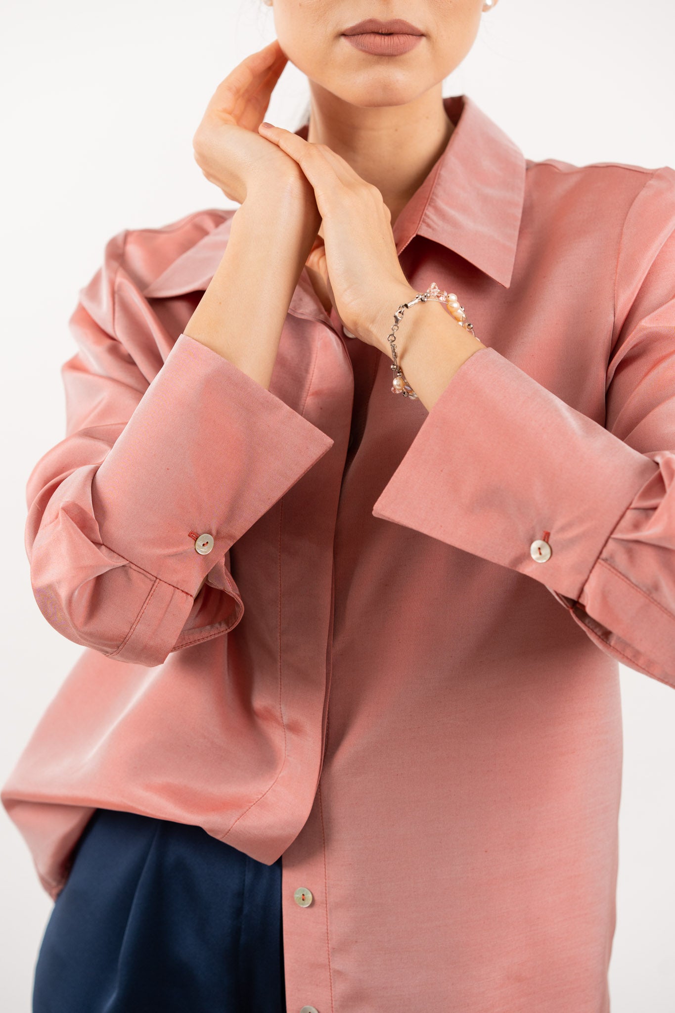 Close-up of peach pink silk shirt, showcasing the lustrous silk fabric, refined stitching, and delicate shell buttons.